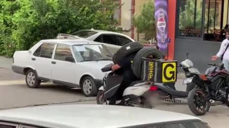 Otomobil lastiğini boynuna asan kuryenin ilginç taşıma yöntemi kameraya yansıdı